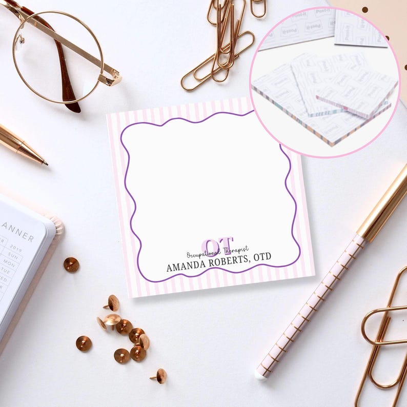 May include: A square notepad with a scalloped purple border and pink striped background. The notepad has the text "OT Occupational Therapist AMANDA ROBERTS, OTD". Other office supplies include a pen, glasses, and paperclips.