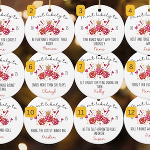 May include: Twelve round white ceramic ornaments featuring a gold string loop. Each ornament displays the text Most likely to, the year 2025, a gold crown, pink and red dice, and hearts. Each ornament includes unique text and a name in red script.