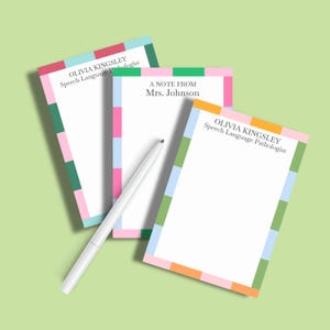 May include: Three white notepads with colorful borders and text. The borders feature a pattern of pink, green, blue, and orange rectangles. One notepad reads "OLIVIA KINGSLEY Speech Language Pathologist", another reads "A NOTE FROM Mrs. Johnson". A white pen rests on the notepads.