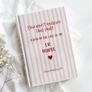 May include: A hardcover book with a light pink and white vertical striped cover. The text reads: You won't believe this shift, A DAY IN THE LIFE OF AN ER NURSE, a red heart, and Olivia Kingsley, RN. The spine features the text CUSTOM SPINE TEXT HERE.