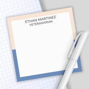 May include: A square notepad with a white center and a border split horizontally between light peach and blue. The text ETHAN MARTINEZ VETERANARIAN is printed in black at the top. A white pen is positioned diagonally across the notepad.
