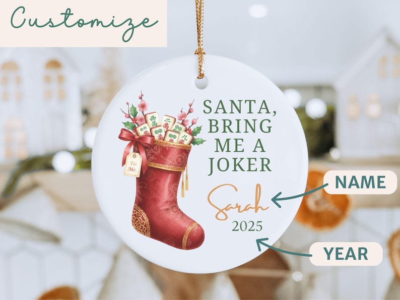 May include: A round white ceramic ornament featuring a red Christmas stocking filled with Mahjong tiles and pink flowers. The text reads SANTA, BRING ME A JOKER, Sarah, and 2025. The ornament hangs from a gold string and includes a gift tag.