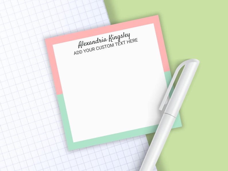 May include: A square notepad with a white center, a pink top border, and a mint green bottom border. The text "Alexandria Kingsley" and "ADD YOUR CUSTOM TEXT HERE" is printed in black at the top. A white pen is positioned next to the notepad.
