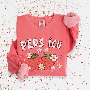 May include: A pink sweatshirt with the text "PEDS ICU" and a graphic of two strawberries with flowers.