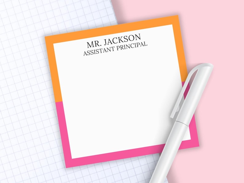May include: A square notepad with a white center and a border split between orange on the top and pink on the bottom. The text MR. JACKSON ASSISTANT PRINCIPAL is printed in black at the top. A white pen is positioned diagonally across the notepad.