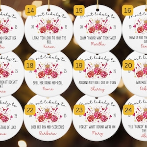 May include: Twelve round white ceramic ornaments featuring a graphic of three red dice with a gold crown, the text Most Likely To, the year 2025, and unique phrases such as Change seats and forget her drink, Laugh too loud, or Win most losses.
