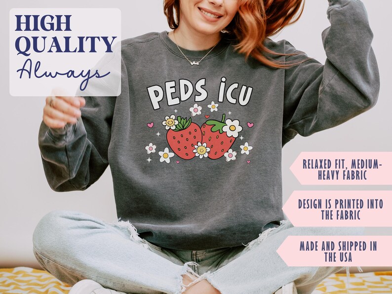 May include: A dark gray sweatshirt with the text "PEDS ICU" in white letters. The text is surrounded by two red strawberries with green leaves and white flowers. The sweatshirt has a relaxed fit and is made of a medium-heavy fabric.