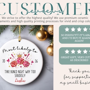 May include: A round white ceramic ornament featuring a graphic of three red dice, a gold crown, and pink hearts. The text reads Most likely to 20 26 TAKE BUNCO NIGHT WAY TOO SERIOUSLY Leslie. The ornament includes a gold hanging string.