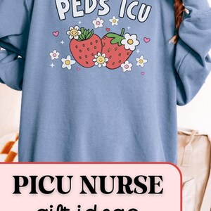 May include: A light blue sweatshirt with the text "PEDS ICU" and a graphic of two strawberries with flowers. The text "PICU NURSE gift ideas" is on a pink banner below the sweatshirt.