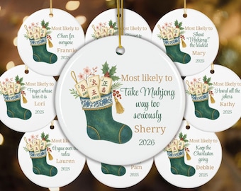 May include: A round white ceramic ornament featuring a green Christmas stocking filled with Mahjong tiles, holly, and berries. The text reads Most likely to Take Mahjong way too seriously, Sherry, and 2026, with a gold hanging string at the top.