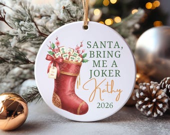 May include: A round white ceramic ornament featuring a red Christmas stocking filled with Mahjong tiles and pink floral sprigs. The text reads: SANTA, BRING ME A JOKER, Kathy, 2026. A small gift tag attached to the stocking says To: Me.