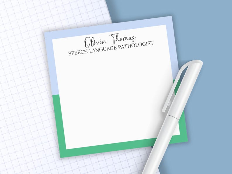 May include: A square notepad with a white center and a border featuring light blue on the top and green on the bottom. The text Olivia Thomas SPEECH LANGUAGE PATHOLOGIST is printed in black at the top. A white pen is positioned next to the notepad.