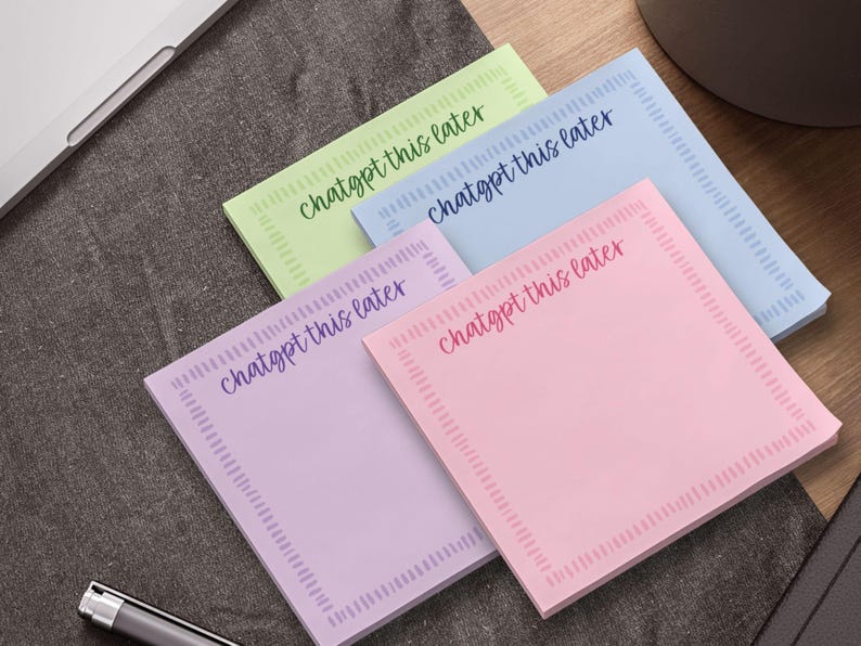 May include: A stack of square sticky notes in pastel colors: green, blue, purple, and pink. Each note has the phrase "chatgpt this later" in a handwritten style font. A pen and laptop are in the background.