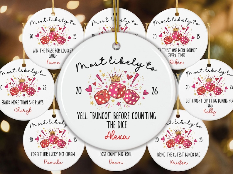 May include: A round white ceramic ornament featuring a graphic of three pink dice, a gold crown, and red hearts. The text reads "Most likely to YELL "BUNCO!" BEFORE COUNTING THE DICE" with the name "Alexa" and the years "20" and "26" printed in black and red.