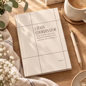 May include: A cream-colored hardcover notebook with a black grid pattern. The cover features the text "CHAOS COORDINATOR" followed by "Turns mayhem into a plan. Keeps the wheels on when everyone else is winging it." and the name "Olivia" in the corner.