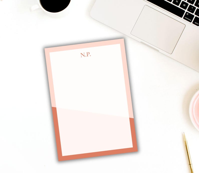 May include: A personalized notepad with a two-tone design. The top and sides are a light pink, while the bottom is a darker coral color. The initials "N.P." are printed in a matching coral color at the top.