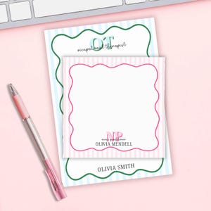 May include: A pink and white striped notepad with a pink scalloped border, with the text "NP nurse practitioner OLIVIA MENDELL". A second notepad with blue and white stripes and green scalloped border has the text "OT occupational therapist OLIVIA SMITH". A pink pen is on the left.
