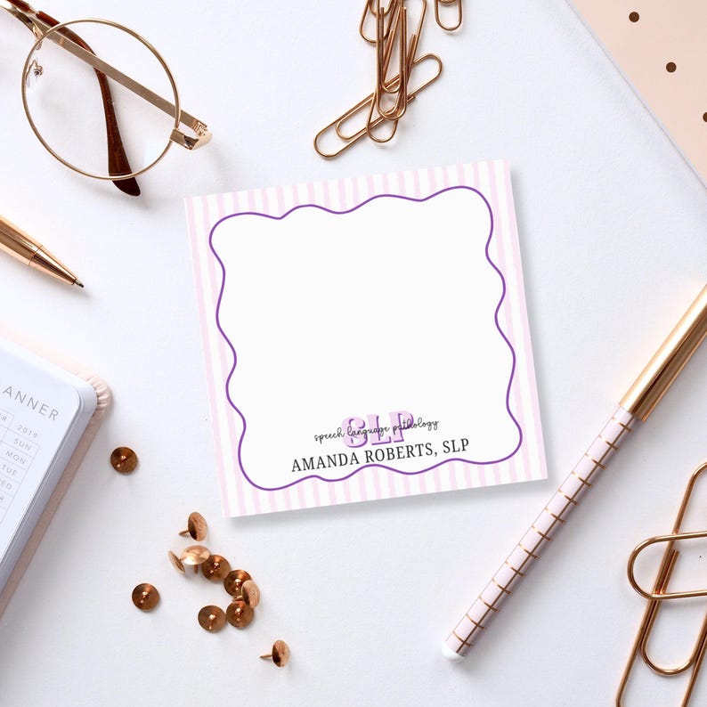 May include: A square notepad with a scalloped purple border and pink vertical stripes. The notepad has the text "SLP speech language pathology" and "AMANDA ROBERTS, SLP" in purple. Gold-colored office supplies surround the notepad.