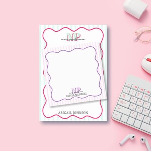 May include: A pink and white striped notepad with a pink and green "NP" logo that says "nurse practitioner". The notepad has a white note card with a pink and purple border and the text "Olivia Mendell" and "Abigail Johnson".