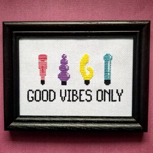 May include: Cross-stitch embroidery with four colorful abstract shapes and the text "GOOD VIBES ONLY" in black thread on a white background.