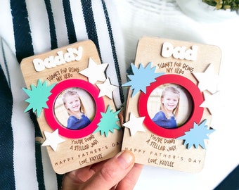 May include: Two wooden photo frames with red, white, and blue stars and a red circle frame. The frames have the text "Daddy Thanks for being my hero" and "Dad Thanks for being my hero". The text "You're doing a stellar job! Happy Father's Day Love, Kaylee" is on both frames.