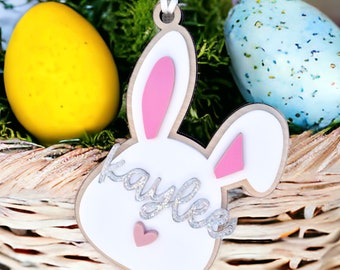 May include: White wooden bunny rabbit Easter ornament with pink ears and a pink heart. The bunny has the name "Kaylee" written in silver glitter on it.
