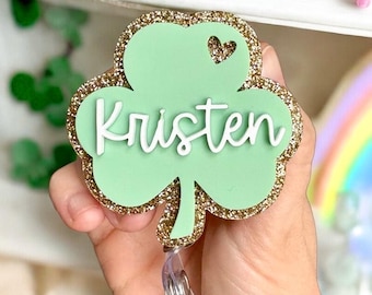 May include: A green shamrock-shaped badge holder with gold glitter trim. The name "Kristen" is written in white on the shamrock.
