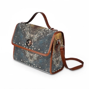 May include: A satchel-style handbag with a flap closure, featuring a unique abstract pattern in shades of blue, gray, and yellow. The bag has brown leather trim, a matching handle, and a detachable shoulder strap. A gold-colored clasp secures the flap.