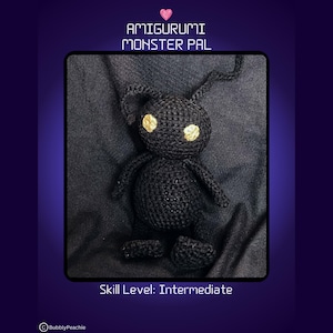 Puede incluir: Amigurumi monstruo amigo negro con ojos amarillos. El amigurumi está sentado sobre un fondo de tela negro. El texto "AMIGURUMI MONSTER PAL" está por encima del amigurumi. El texto "Nivel de habilidad: Intermedio" está debajo del amigurumi.