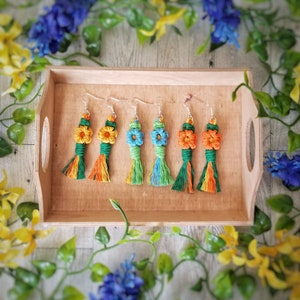 May include: Five pairs of crocheted flower earrings with tassels. The earrings are in shades of green, blue, orange, and yellow.
