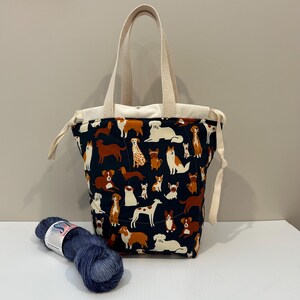 May include: A navy blue tote bag with a white canvas handle and a pattern of colourful dogs. The bag has a drawstring closure and is made of a durable fabric.