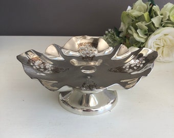 May include: A silver decorative serving dish with a scalloped edge and a pedestal base. The dish has a floral design.
