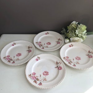 Peut inclure: Quatre assiettes plates en céramique blanche avec un bord doré et un motif floral de roses roses.