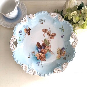May include: A vintage blue and white porcelain serving platter with a floral design of brown leaves and purple berries. The platter has a scalloped edge and two handles.