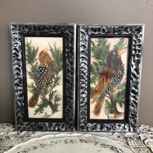 May include: Two framed bird illustrations with black frames and a distressed silver finish. The birds are depicted in a woodland setting with green foliage. The birds are made of feathers and have black and white markings.