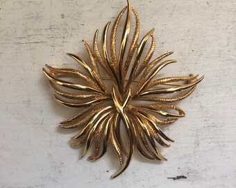 May include: A gold-toned brooch in the shape of a stylized flower with a textured finish.