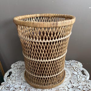 May include: A tall, woven wicker basket with a flared top and a round base. The basket features a diamond pattern and is made of light brown wicker. The basket is likely used for storage or decorative purposes.