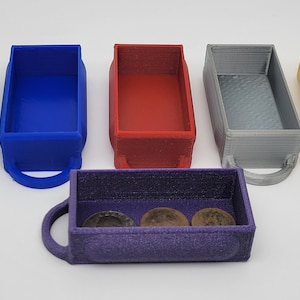 May include: Six small, rectangular storage containers with handles. The containers are made of plastic and are in various colors: green, blue, red, gray, gold, and purple. The purple container has three coins inside.