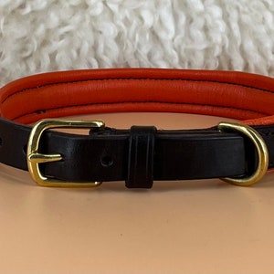 May include: A black leather dog collar with an orange leather lining and a brass buckle.