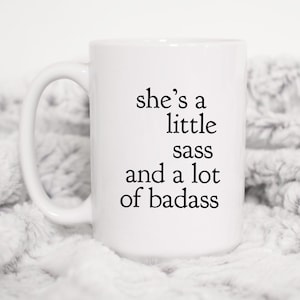 May include: White ceramic mug with black text that reads "she's a little sass and a lot of badass".
