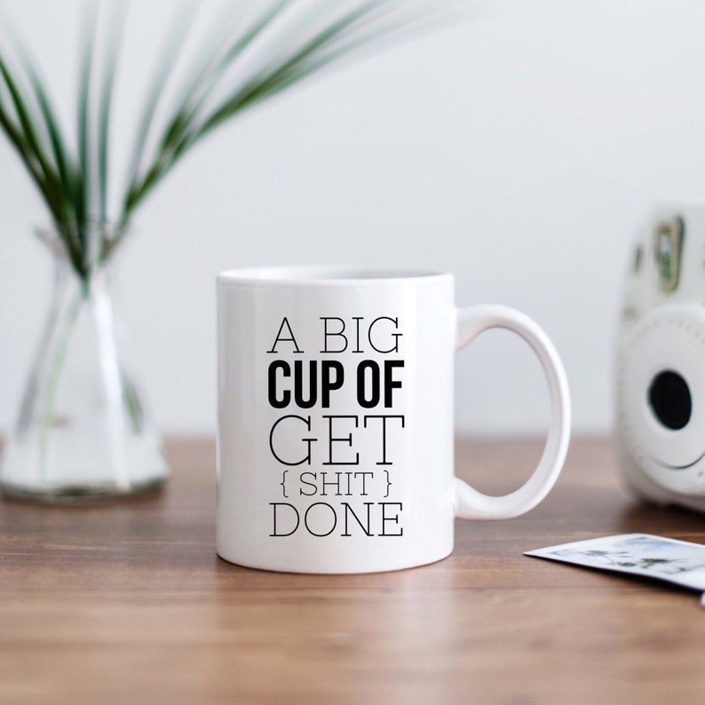 May include: White ceramic coffee mug with black text that reads "A big cup of get {shit} done".