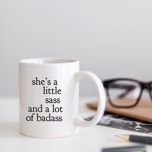 May include: White ceramic mug with black text that reads "she's a little sass and a lot of badass".