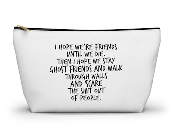 May include: A white zippered pouch featuring black text that reads: I HOPE WE'RE FRIENDS UNTIL WE DIE. THEN I HOPE WE STAY GHOST FRIENDS AND WALK THROUGH WALLS AND SCARE THE SHIT OUT OF PEOPLE. The pouch has a gold-toned zipper pull at the top corner.