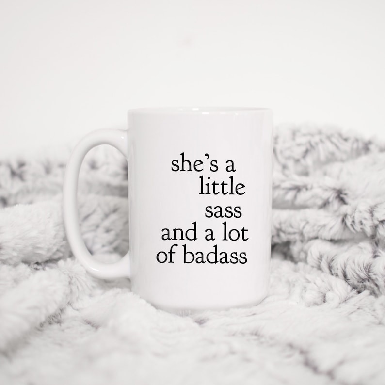 May include: White ceramic mug with black text that reads "she's a little sass and a lot of badass".