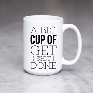 May include: White ceramic coffee mug with black text that reads "A big cup of get {shit} done".