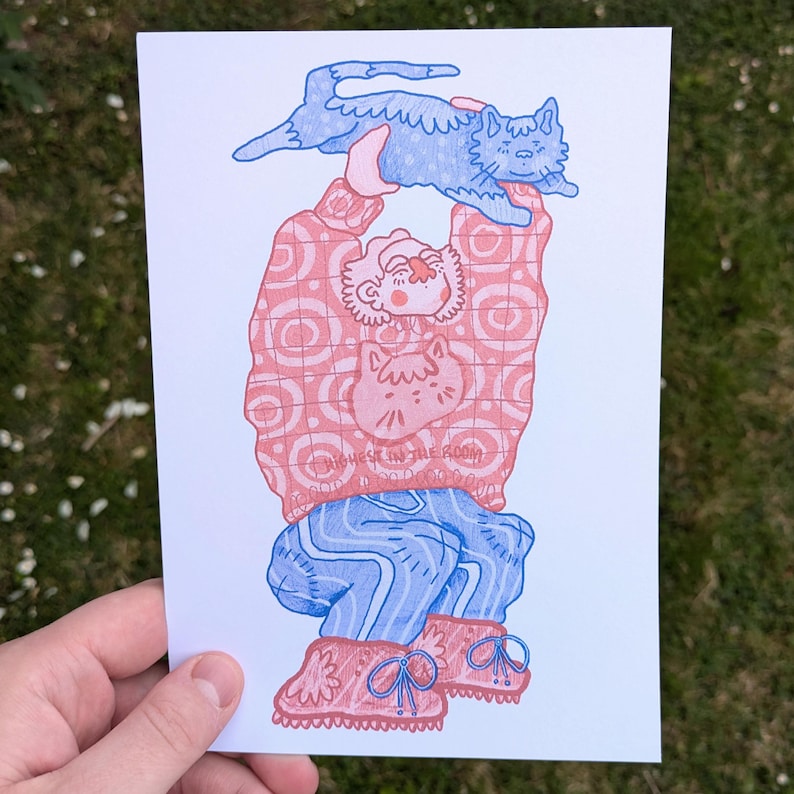 Op de afbeelding: Illustratie van een persoon die een blauwe kat boven zijn hoofd houdt. De persoon draagt een roze trui met een kattenafbeelding en een blauwe broek. De tekst "HIGHEST IN THE ROOM" is zichtbaar op de trui.