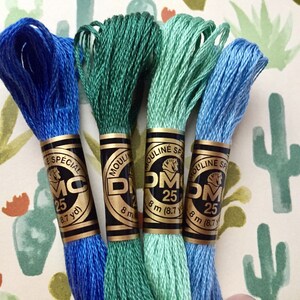 May include: Four spools of DMC embroidery floss in shades of blue and green. The spools are labeled "Mouline Special" and "DMC 25" with the length in yards and meters.