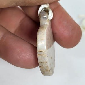 Puede incluir: Un colgante de coraz&oacute;n blanco y marr&oacute;n con un cord&oacute;n plateado.