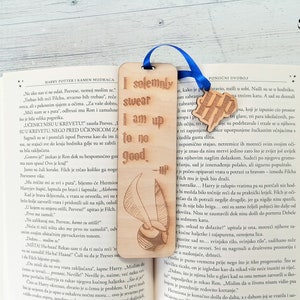May include: A wooden bookmark featuring a Harry Potter themed design. The bookmark is brown with a gold-coloured design of a golden snitch and the text "I solemnly swear I am up to no good." The bookmark is attached to a blue ribbon.