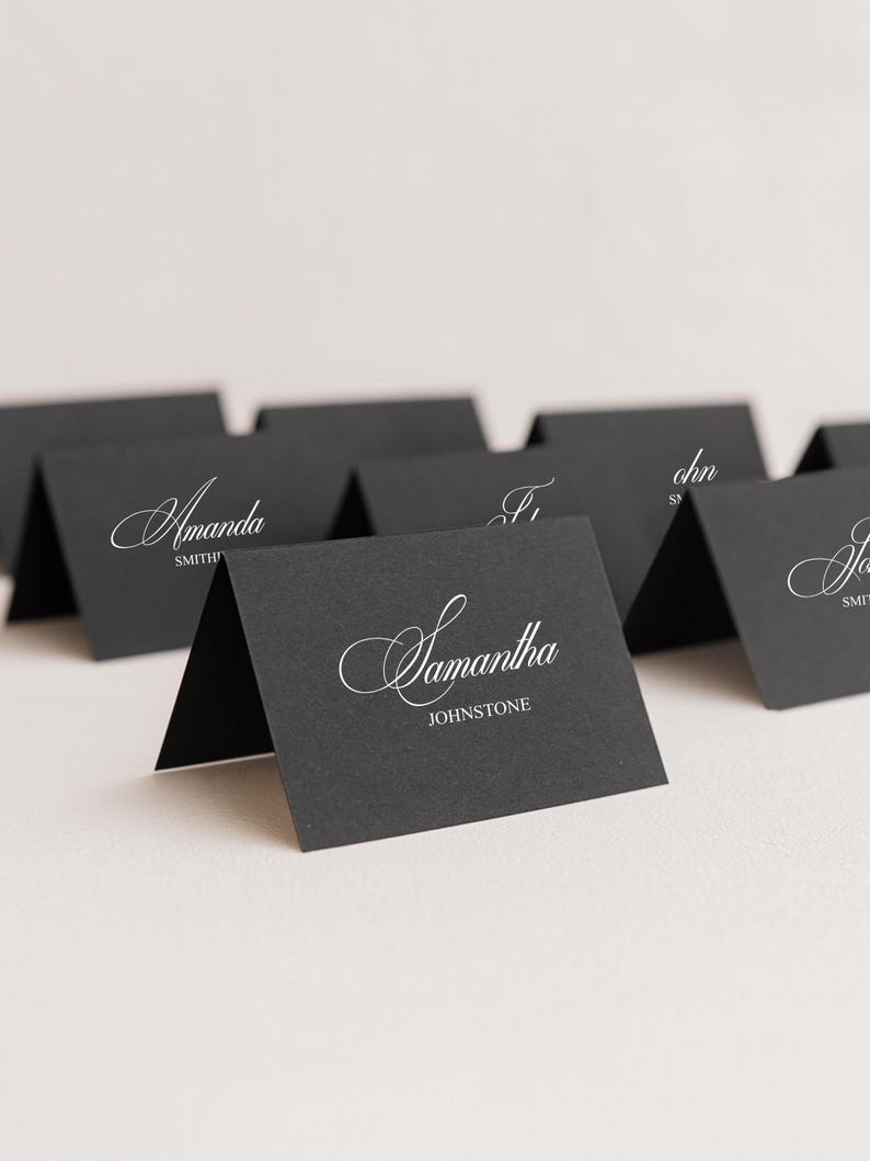 May include: Black place cards with white calligraphy names. The cards are folded and stand upright. The name "Samantha Johnstone" is visible on one card. Other cards have names like "Amanda Smith".